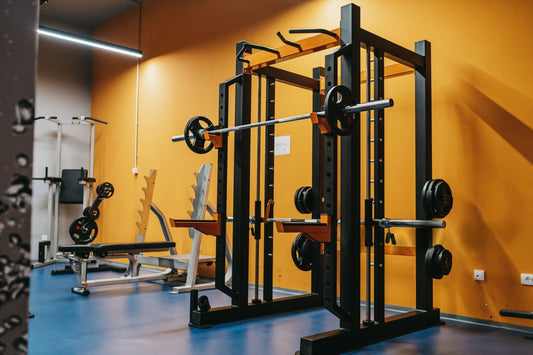 A gym interior featuring a barbell with weights on a rack, surrounded by exercise equipment and mats.