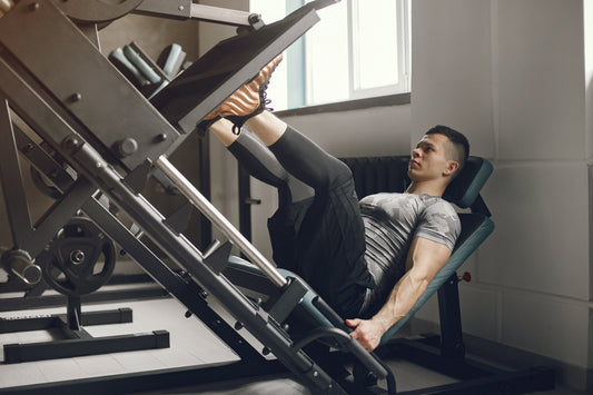 A man sits on a front squat machine, actively participating in a workout at the gym.