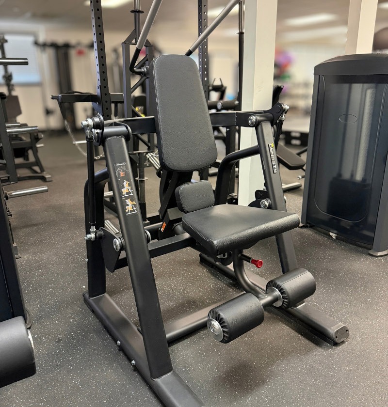 A black plate loaded ab crunch gym machine photographed inside a fitness center, with other exercise equipment visible in the blurred background.
