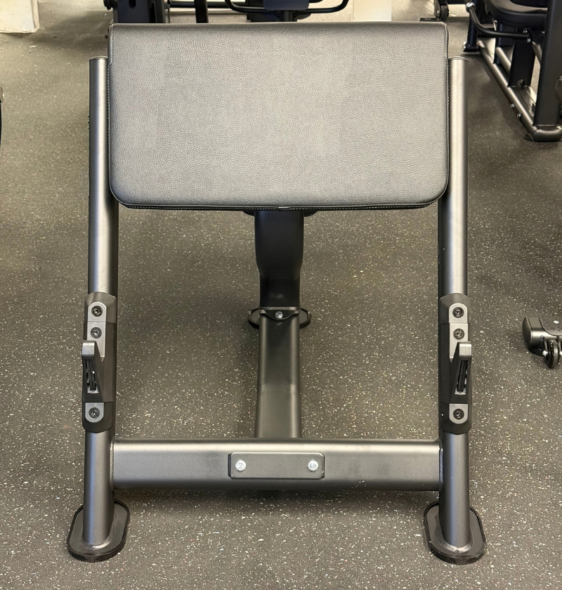 A close-up view of a preacher bench, showing the black padded seat, dark gray metal frame, and adjustment levers on the front legs, set on a speckled gray gym floor.