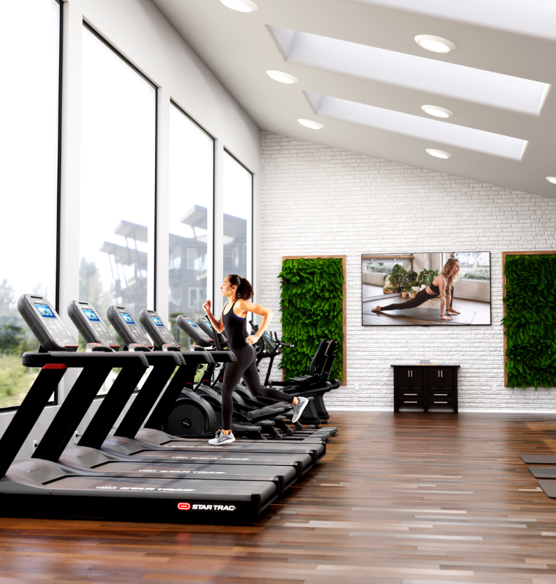 Woman running on a treadmill in a modern gym with large windows and fitness-themed decor.