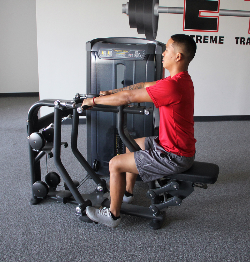 In a gym, a man engages in Compound Rows using a machine, emphasizing his workout routine and fitness goals.